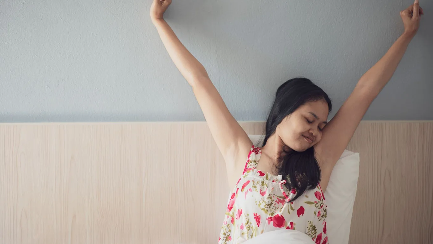 A woman joyfully stretching her arms while waking up in bed, feeling refreshed and energized.