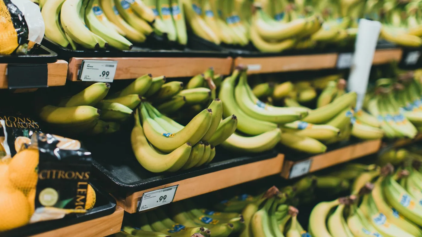 Close-up of fresh bananas stacked on grocery store shelves with price tags visible.