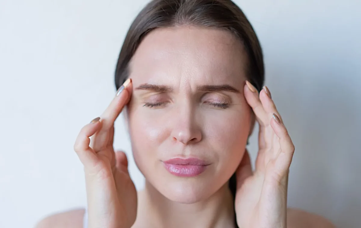 Close-up of a woman with closed eyes holding her temples, showing signs of a migraine or headache.