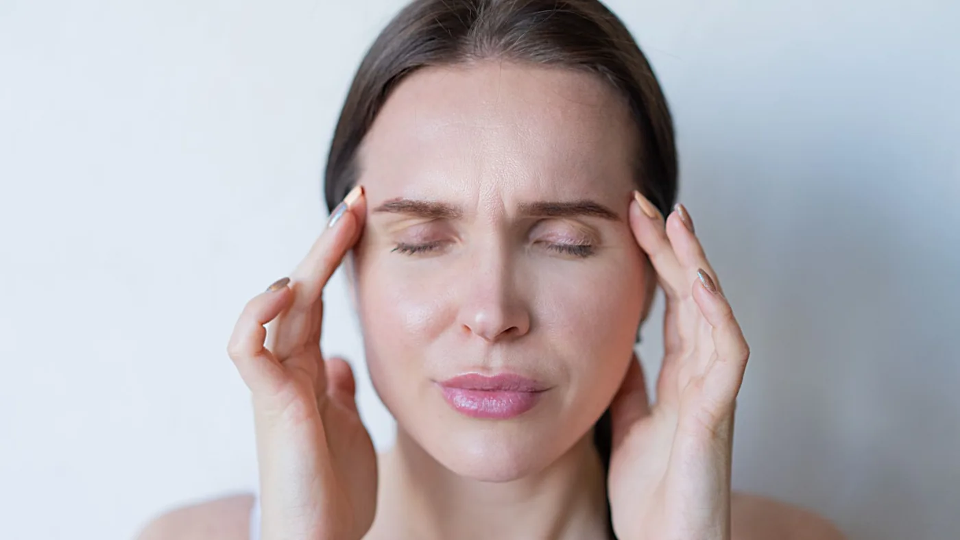 Close-up of a woman with closed eyes holding her temples, showing signs of a migraine or headache.