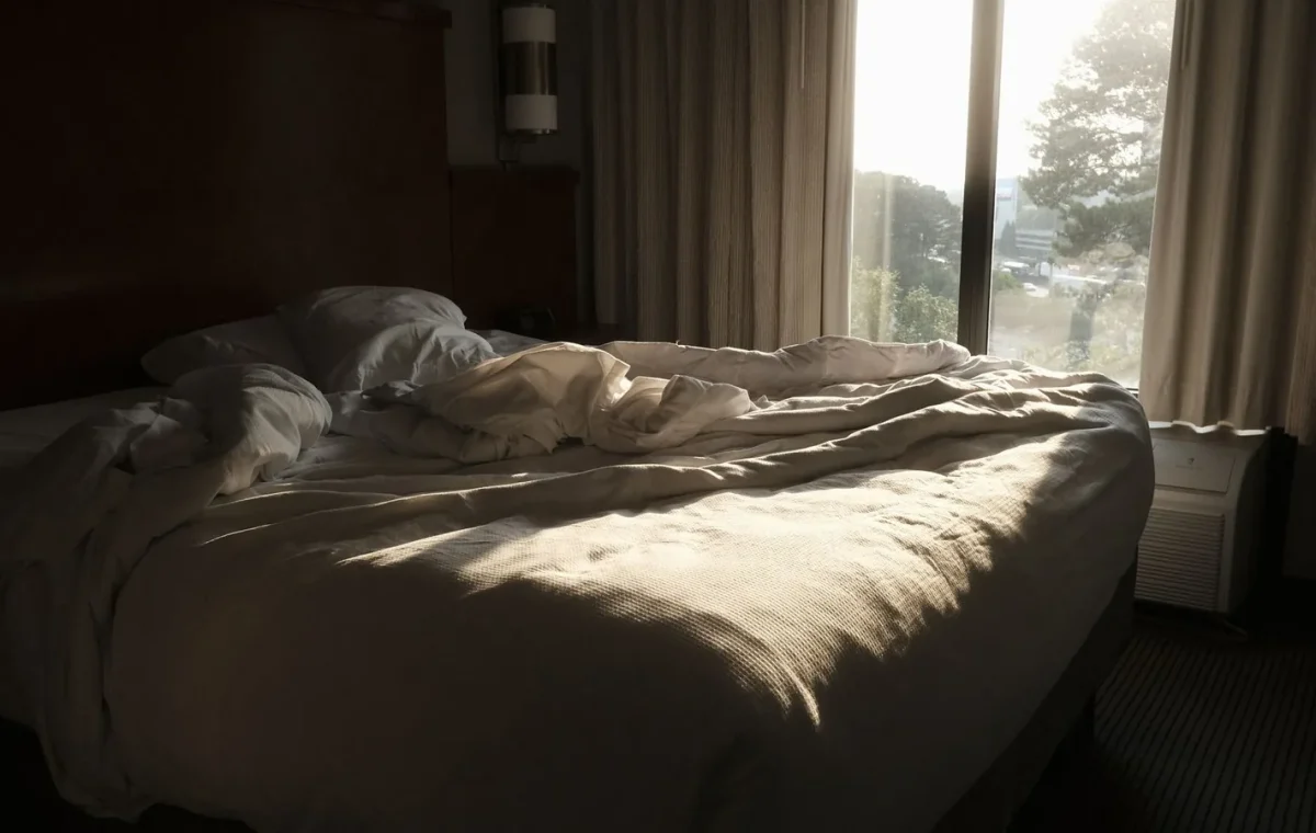 A comfortable bed in a bedroom with soft morning sunlight illuminating the room.