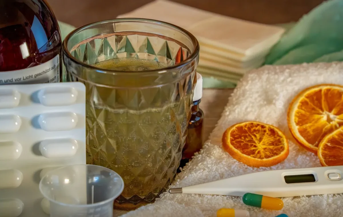 A collection of home remedies and medications for treating cold and flu symptoms, including a thermometer, pills, and herbal tea.