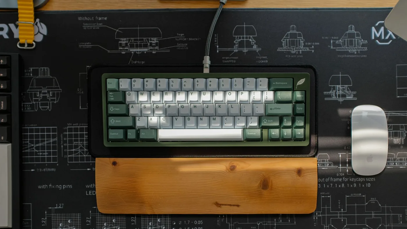 Top view of an ergonomic keyboard setup on a designer desk with a wooden wrist rest and blueprint-themed mouse pad.