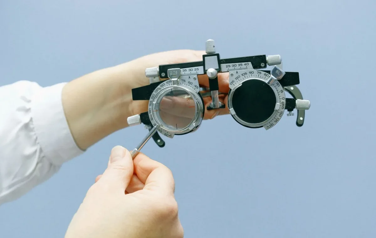 Crop anonymous ophthalmologist setting eye vision test glasses with magnifying glass and numeral scale in blue background