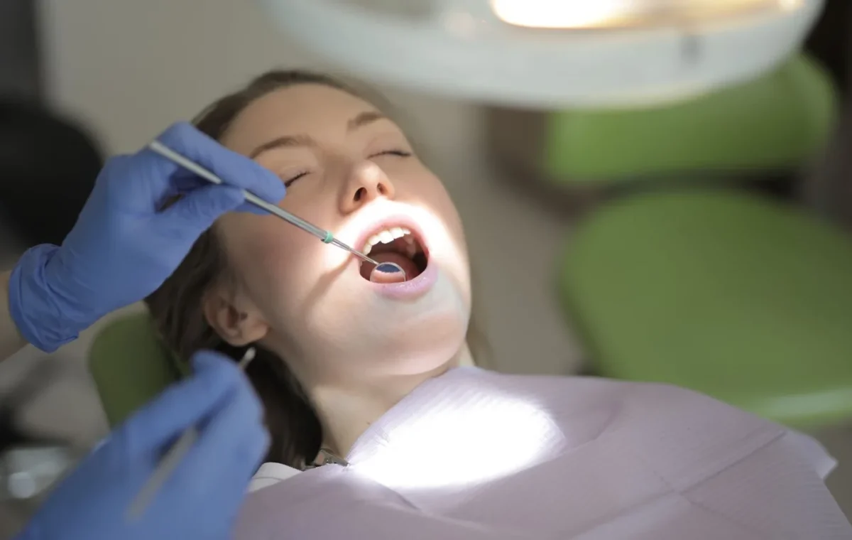 From above view of crop unrecognizable dentist in latex gloves using medical instruments while examining teeth of patient during work in modern dental room
