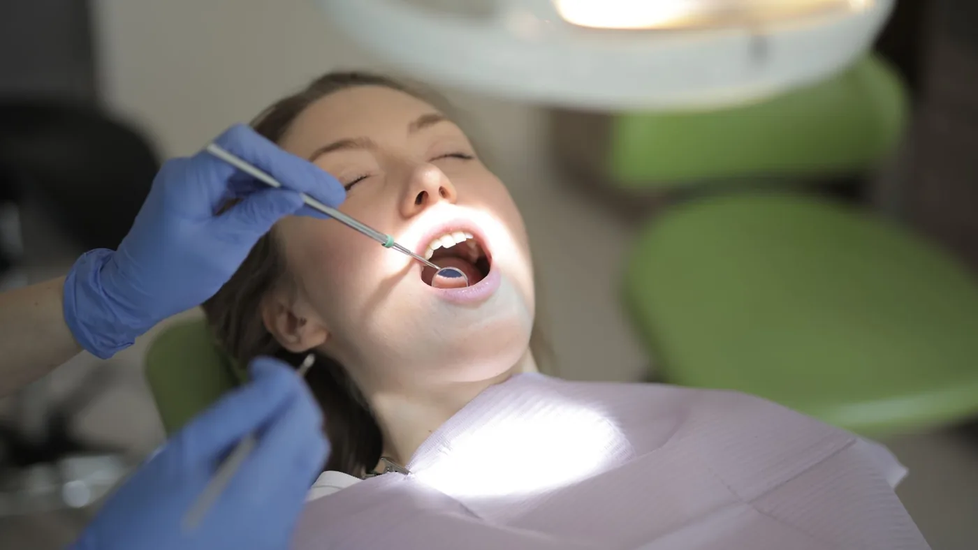 From above view of crop unrecognizable dentist in latex gloves using medical instruments while examining teeth of patient during work in modern dental room