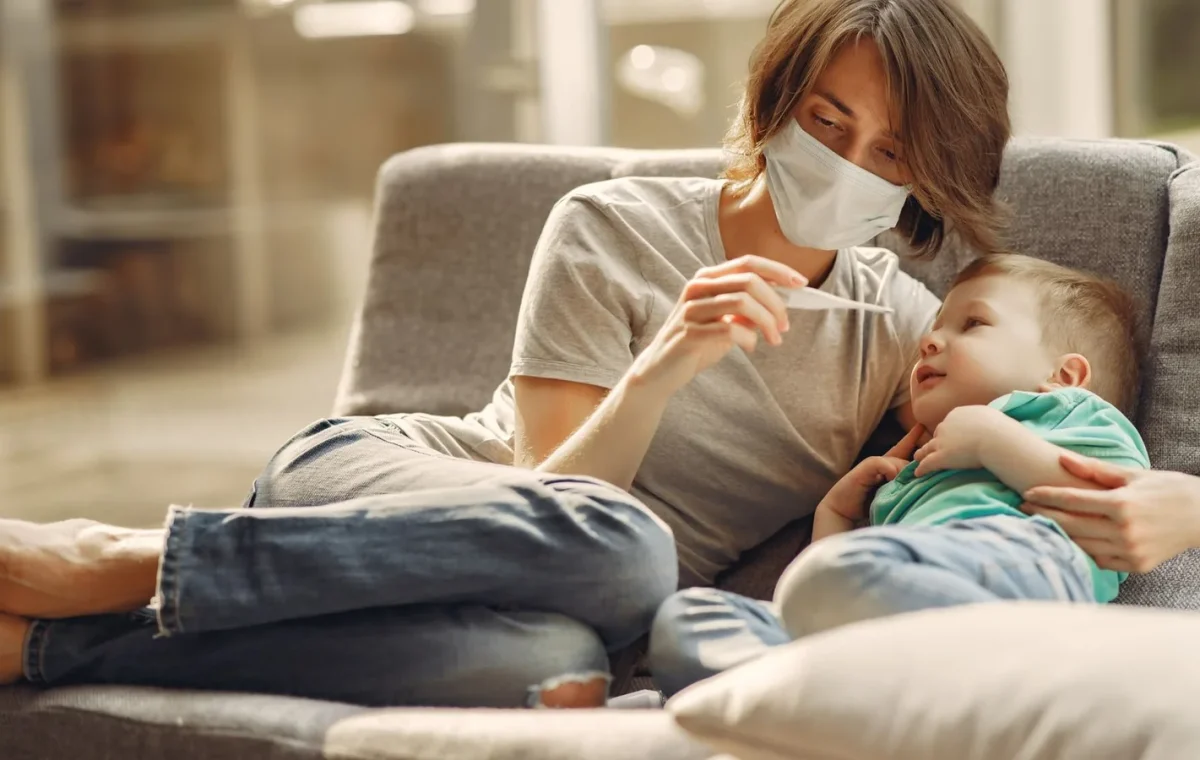 A caring mother checks her son's temperature while they relax on a sofa, showcasing parent-child affection and health care.