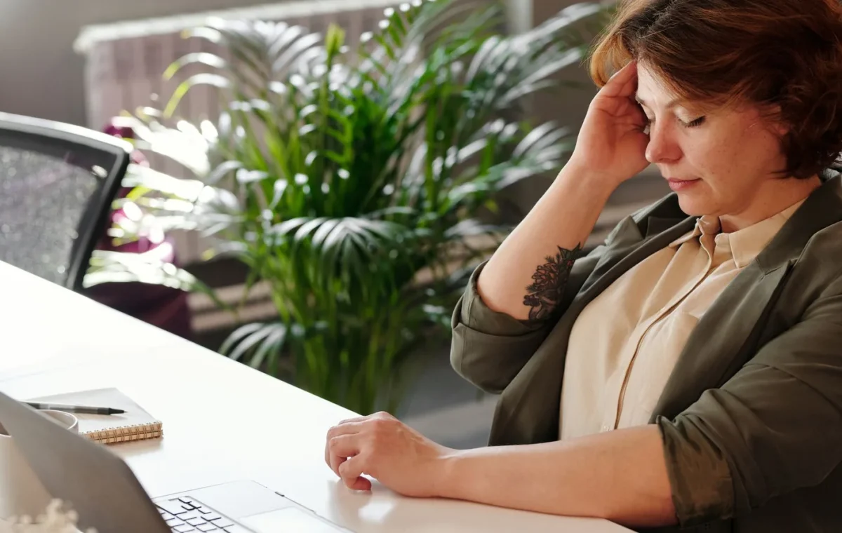A businesswoman feeling stressed at her home office desk while working on her laptop.