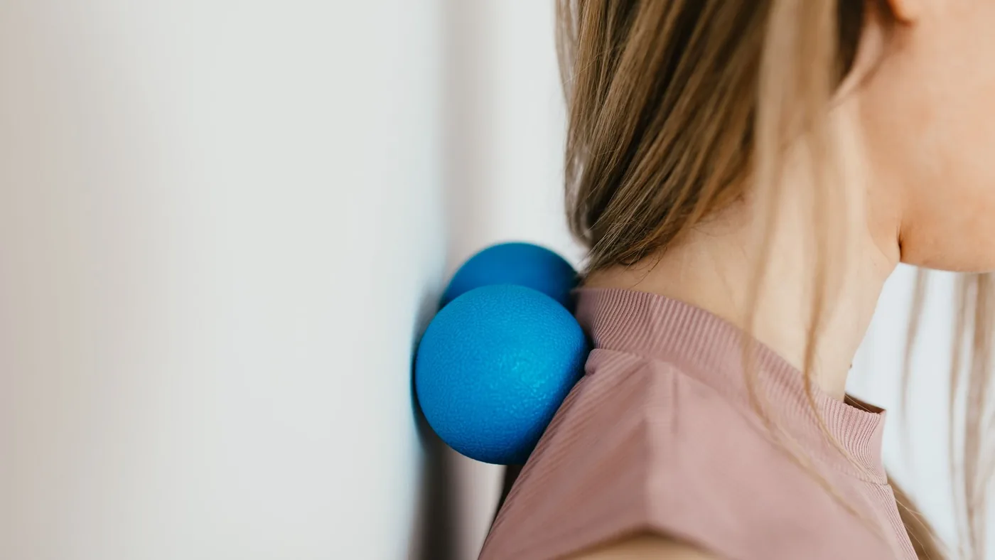 Side view crop unrecognizable female leaning on small balls against wall to massage stiff neck muscles and sore neck