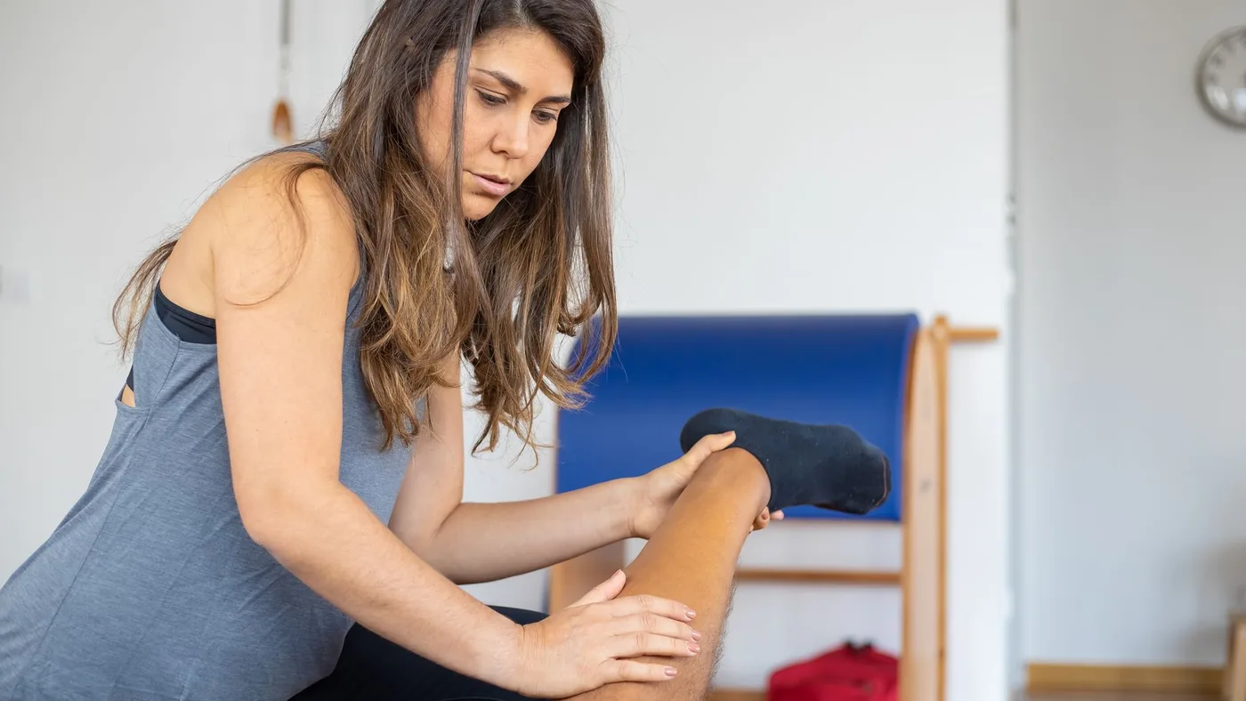 A female trainer assists a client with leg stretching indoors. Focus on fitness and flexibility training.