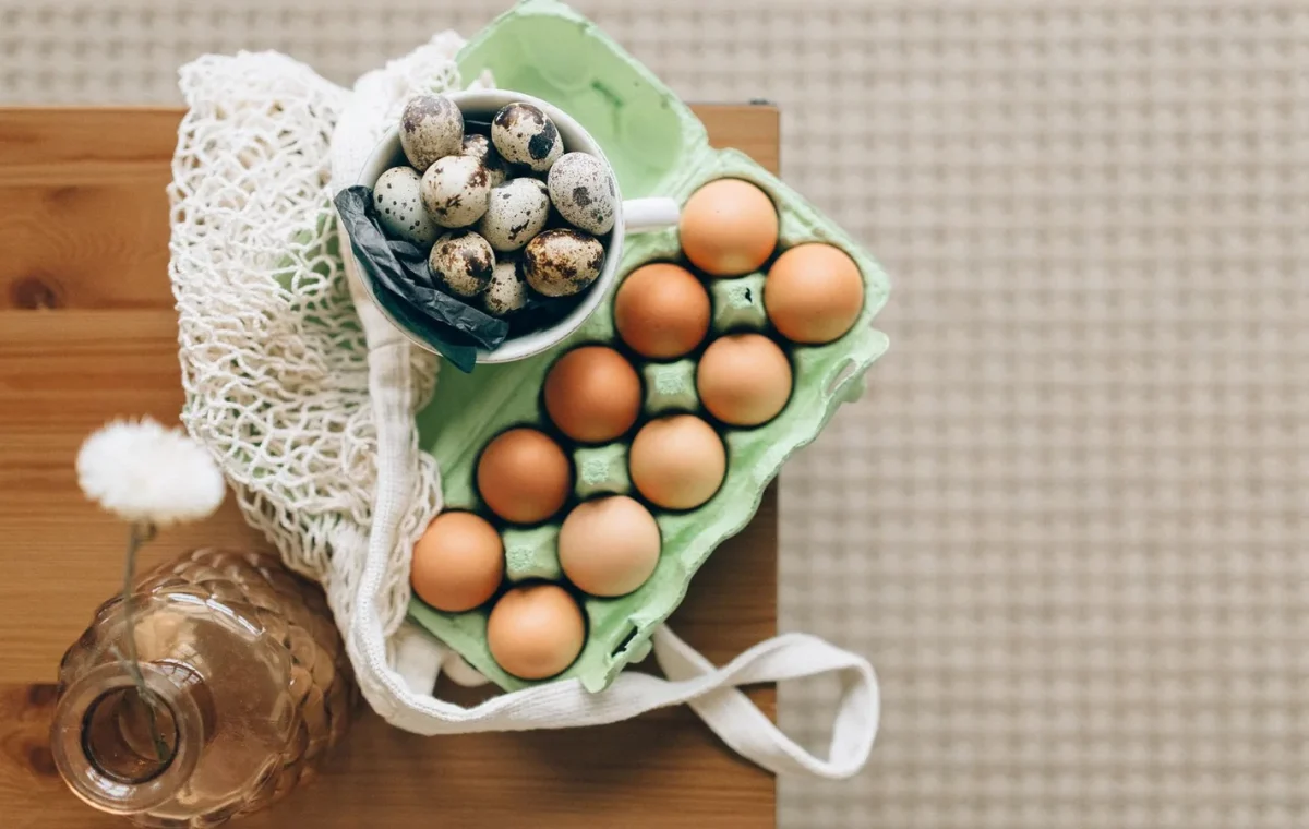 Top view of quail and chicken eggs in carton on a wooden table with organic produce vibe.