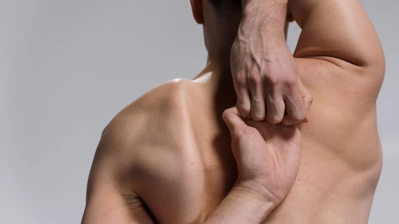 Shirtless muscular man practicing a yoga stretch with hands clasped behind back on a white background.