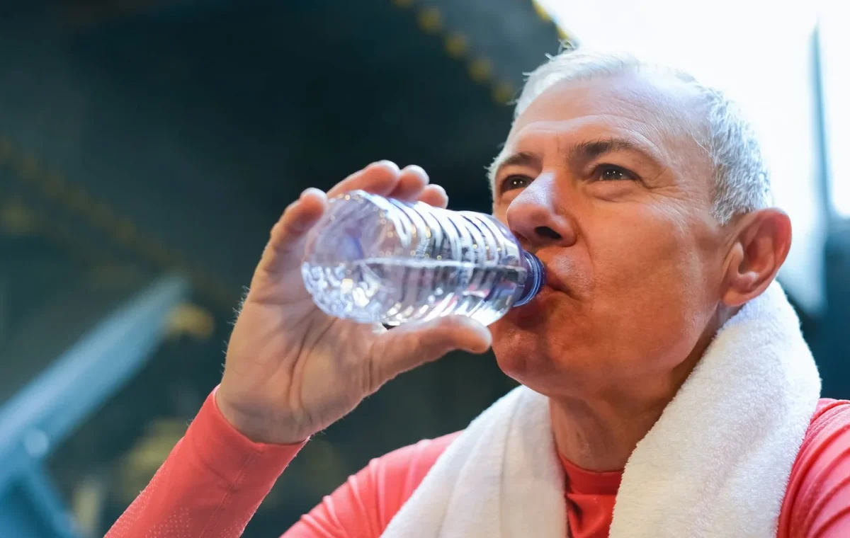 Elderly man drinking water post-exercise with towel around neck, promoting healthy lifestyle.
