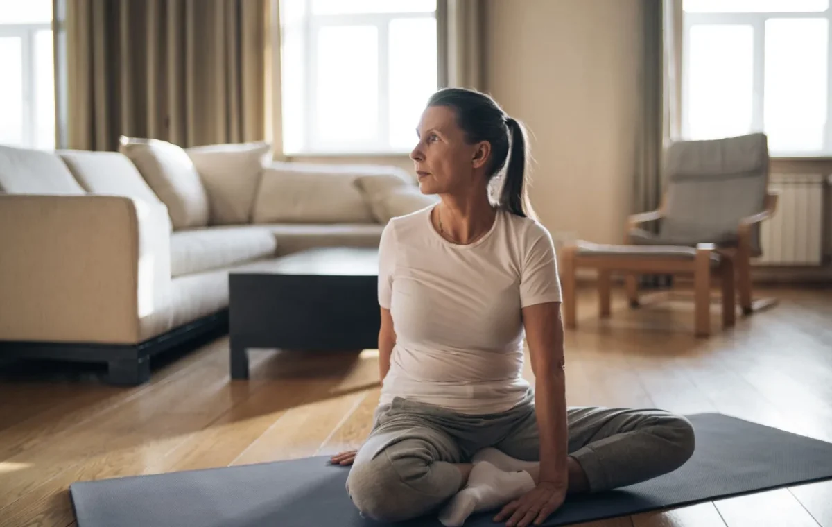 Senior woman doing yoga in a living room, promoting healthy lifestyle and positive aging.