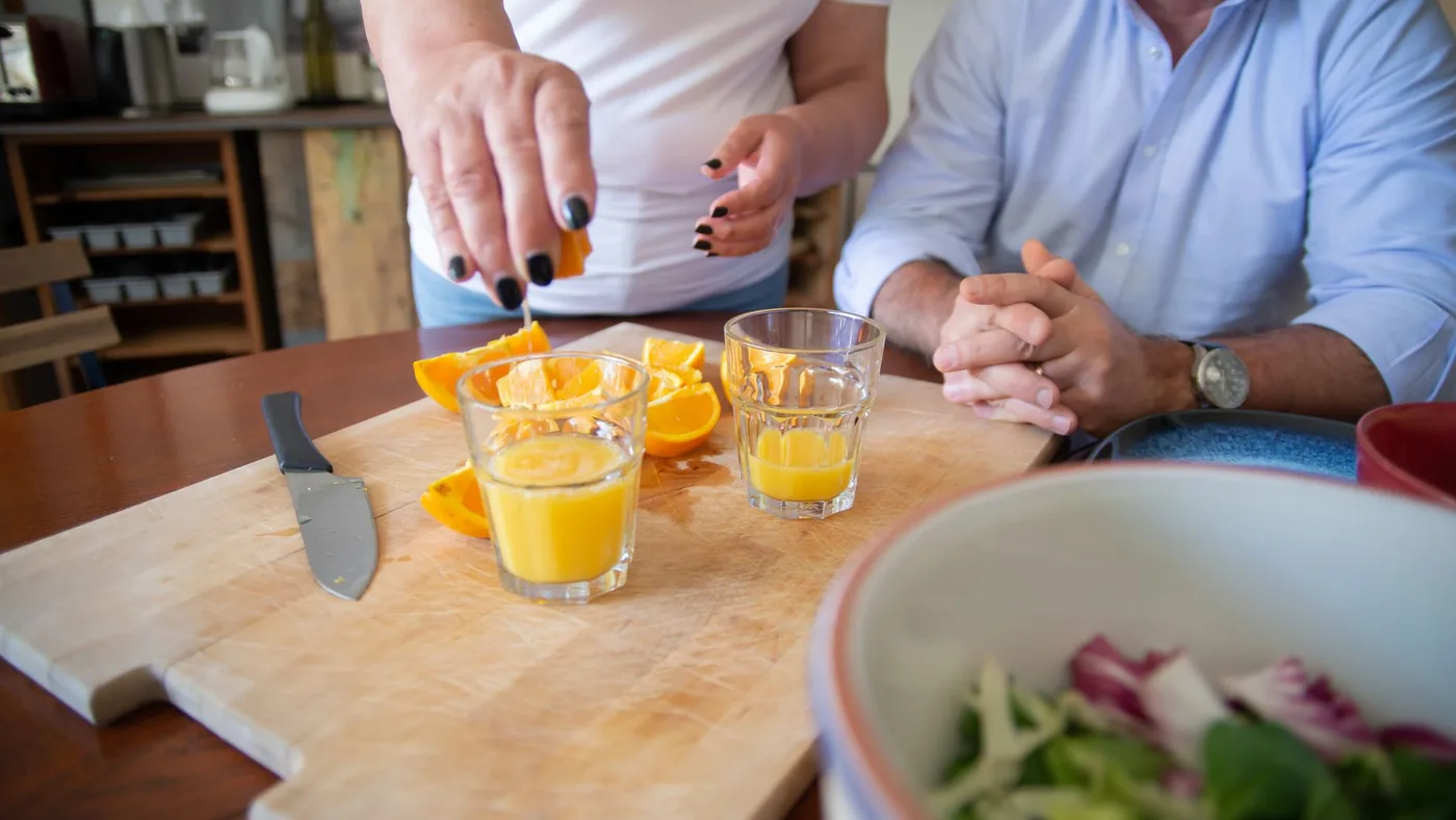 Hands squeezing fresh orange juice on a chopping board indoors with drinking glasses.