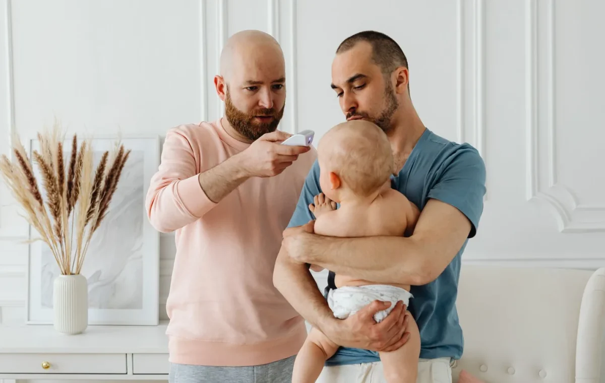 A worried father checks baby's temperature while partner holds the child at home.