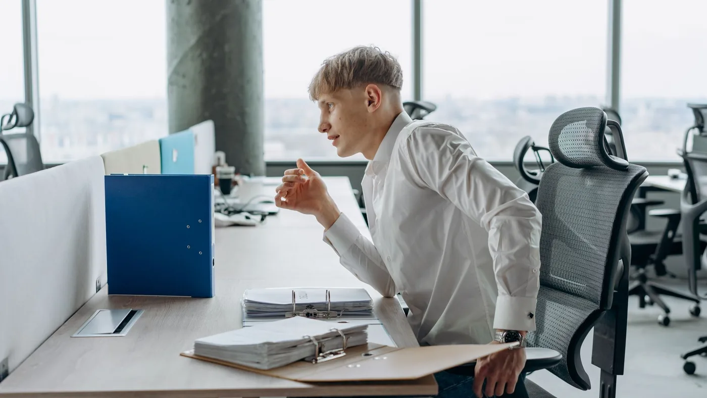 Young man in white shirt working at an office desk with files in a modern workplace.