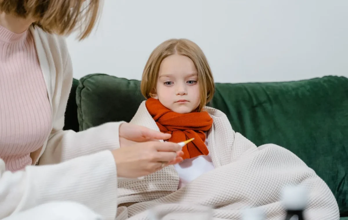 A caring moment of a woman checking a sick child's temperature on a cozy green couch indoors.