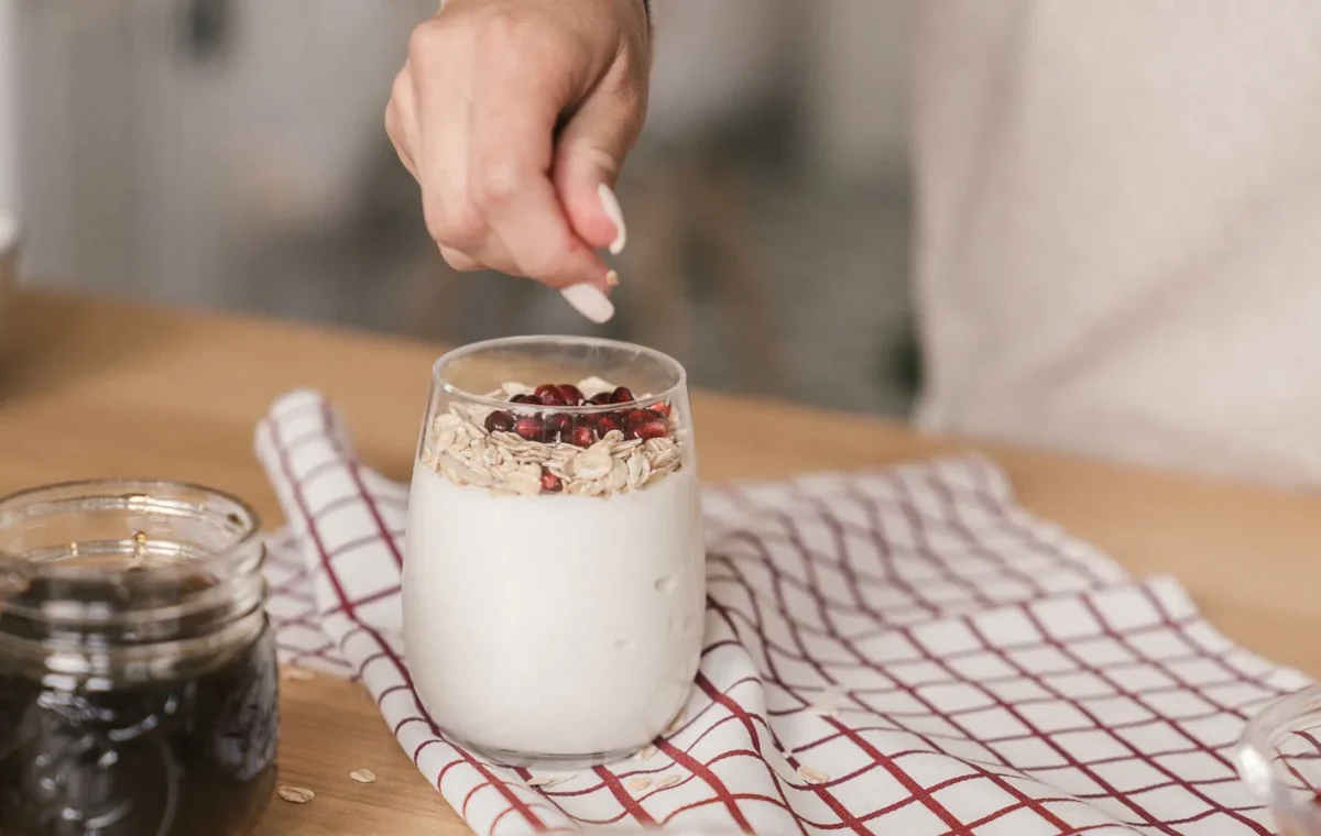 Person preparing yogurt with granola and pomegranate. A nutritious and delicious breakfast idea.