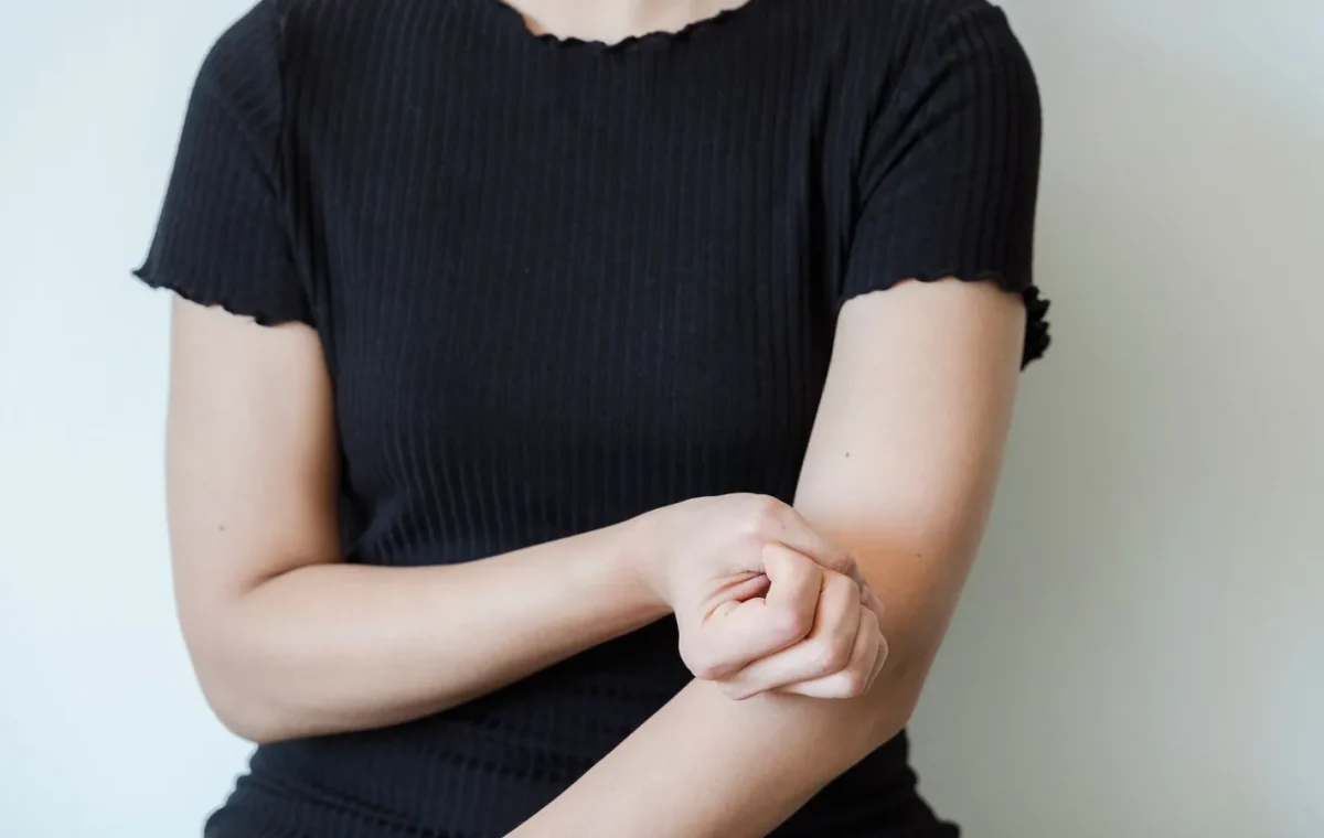 A close-up view of a woman in a black shirt holding her arm, showcasing skin contact and emotion.