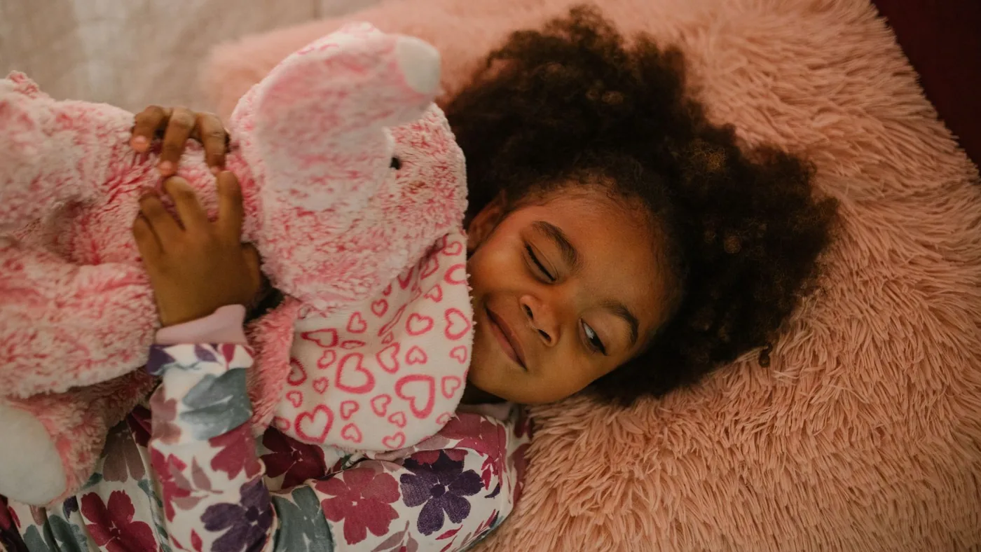 Child in pajamas hugging a stuffed elephant, enjoying a cozy bedtime moment.