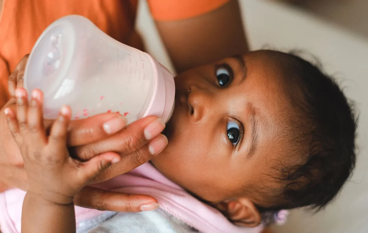 Close-up of a mother feeding her baby with a milk bottle indoors.