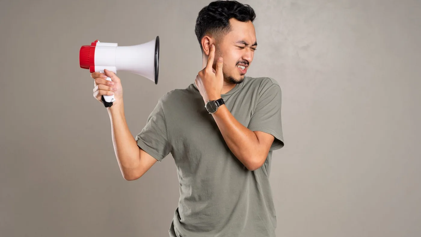 A man with a megaphone holding ear in discomfort, representing noise pollution or loud sounds.