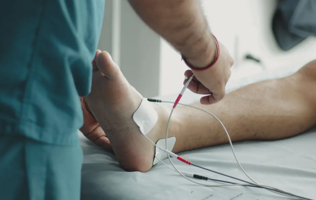 Close-up of a healthcare worker examining a patient's foot with medical equipment in a hospital setting.