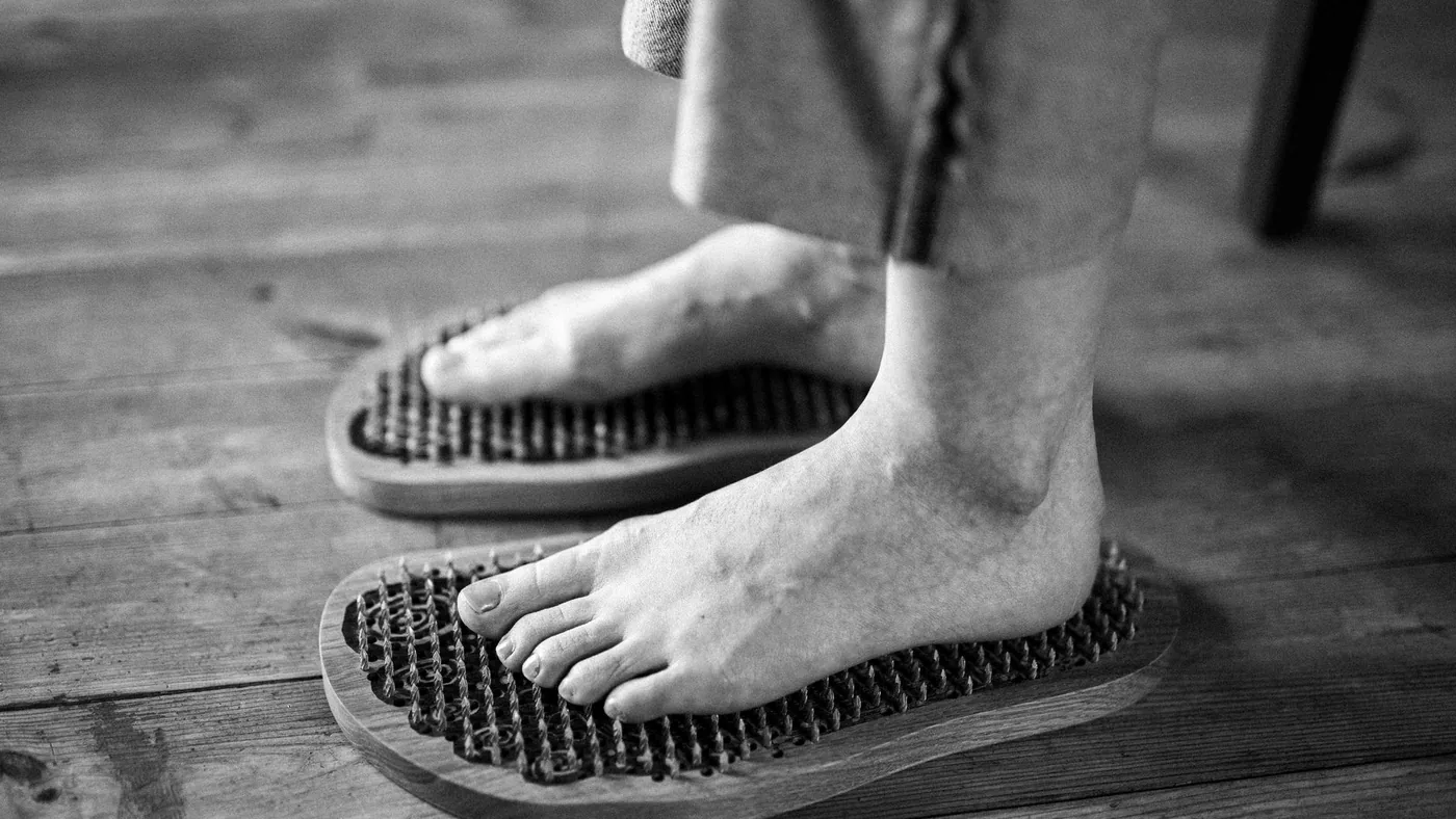 Black and white photo of feet receiving a relaxing massage on wooden reflexology boards.