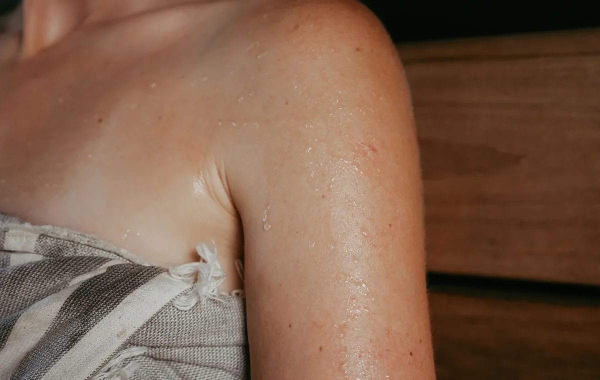Close-up of a woman with sweat on her skin inside a sauna, highlighting relaxation and wellness.