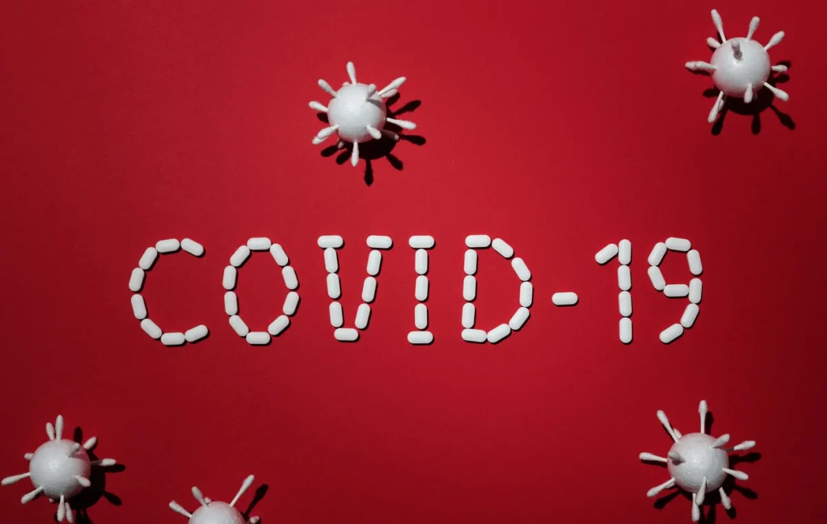 Artistic representation of COVID-19 using pills and virus models on red background.