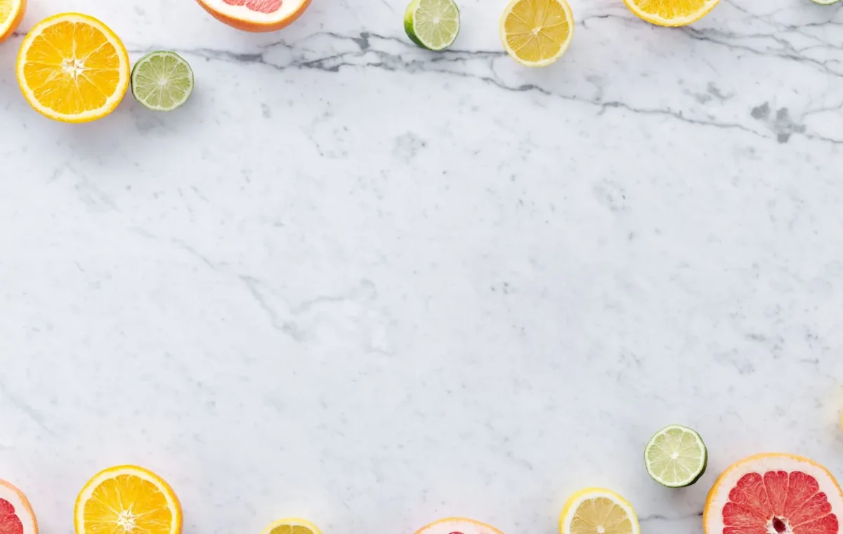 Flat lay of assorted citrus slices on a marble surface with ample copy space.