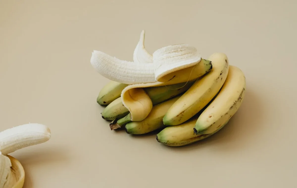 A bunch of ripe bananas with one peeled, displayed on a neutral backdrop. Ideal for food visuals.