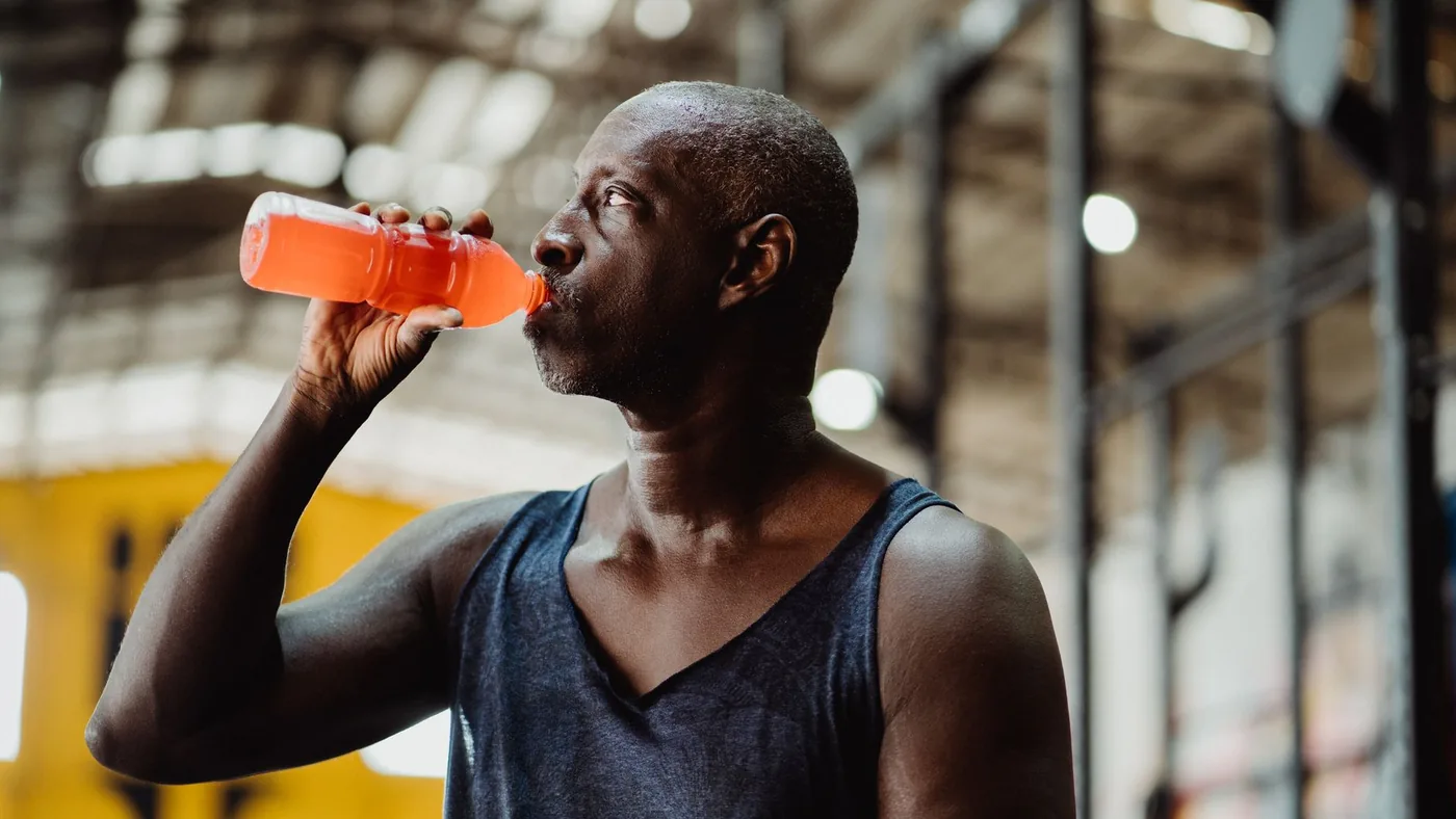 An athletic man enjoys a refreshing energy drink during his workout in a gym setting.