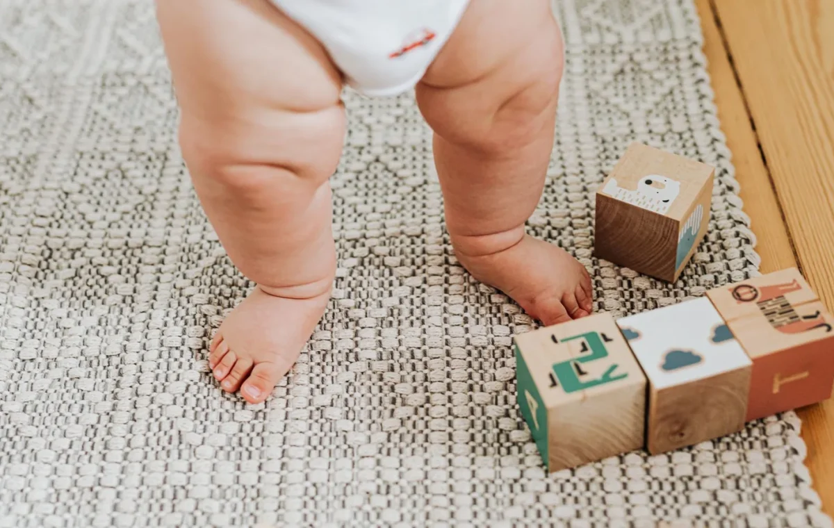 Capturing a baby's first steps with wooden building blocks on a soft indoor rug. Perfect for childhood memories.