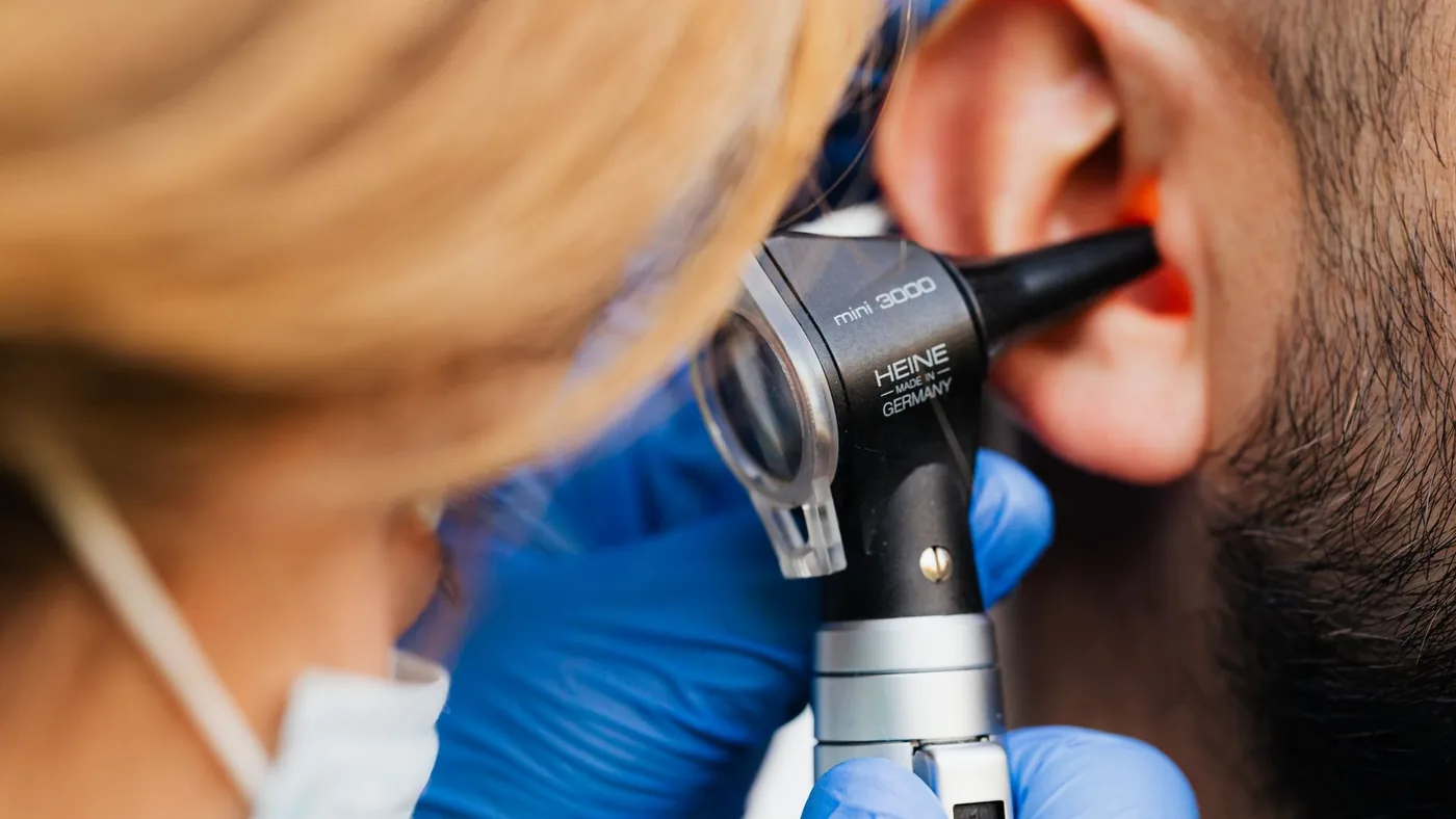 A medical professional examines a patient's ear using a Heine otoscope, highlighting healthcare quality.