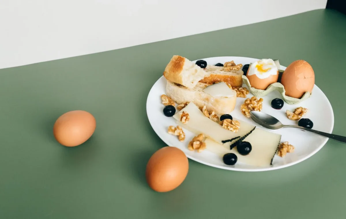 Plate of cheese, boiled eggs, bread, walnuts, and blueberries for a hearty breakfast.
