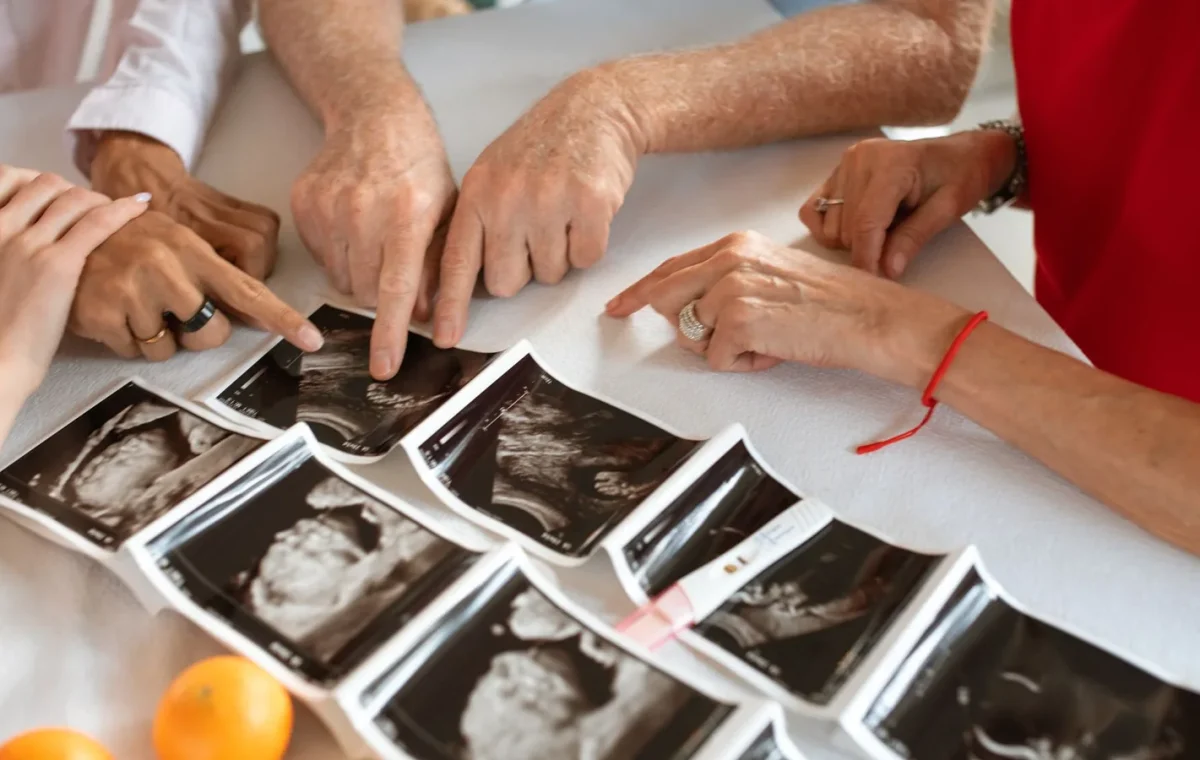 A group of adults pointing at ultrasound images on a table, symbolizing family and anticipation.