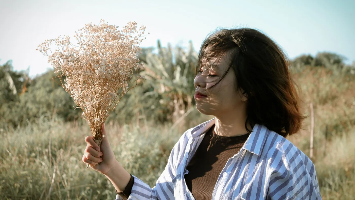 A happy Asian woman holds a bouquet of wildflowers in a sunny outdoor setting.