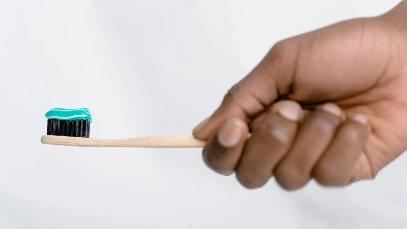 Hand holding a bamboo toothbrush with green toothpaste, focusing on oral hygiene.