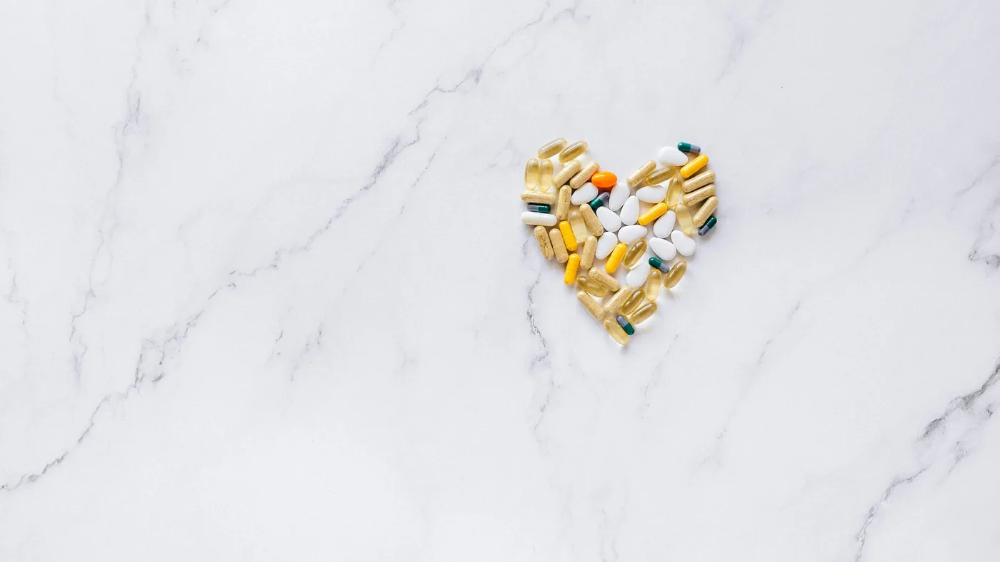 Colorful pills arranged in a heart shape on a marble surface, symbolizing healthcare and well-being.