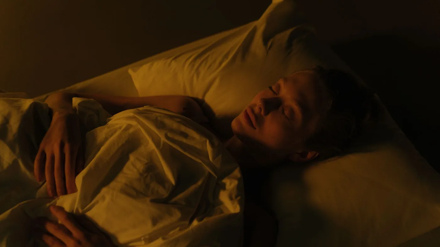 A woman peacefully sleeping in a dimly lit bedroom, wrapped in a white blanket.