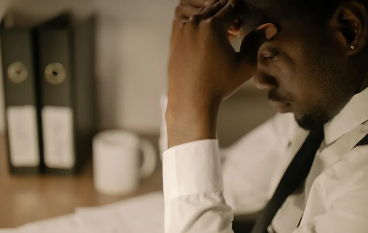 Side view of a stressed businessman in white shirt holding head at a desk with papers.