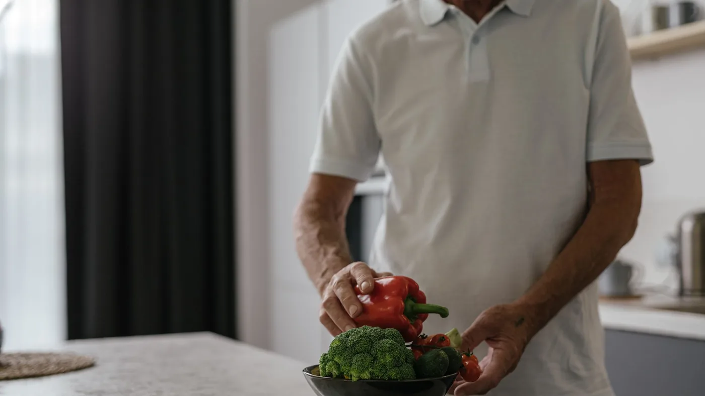 Elderly man in kitchen holding vegetables, embracing a healthy lifestyle.