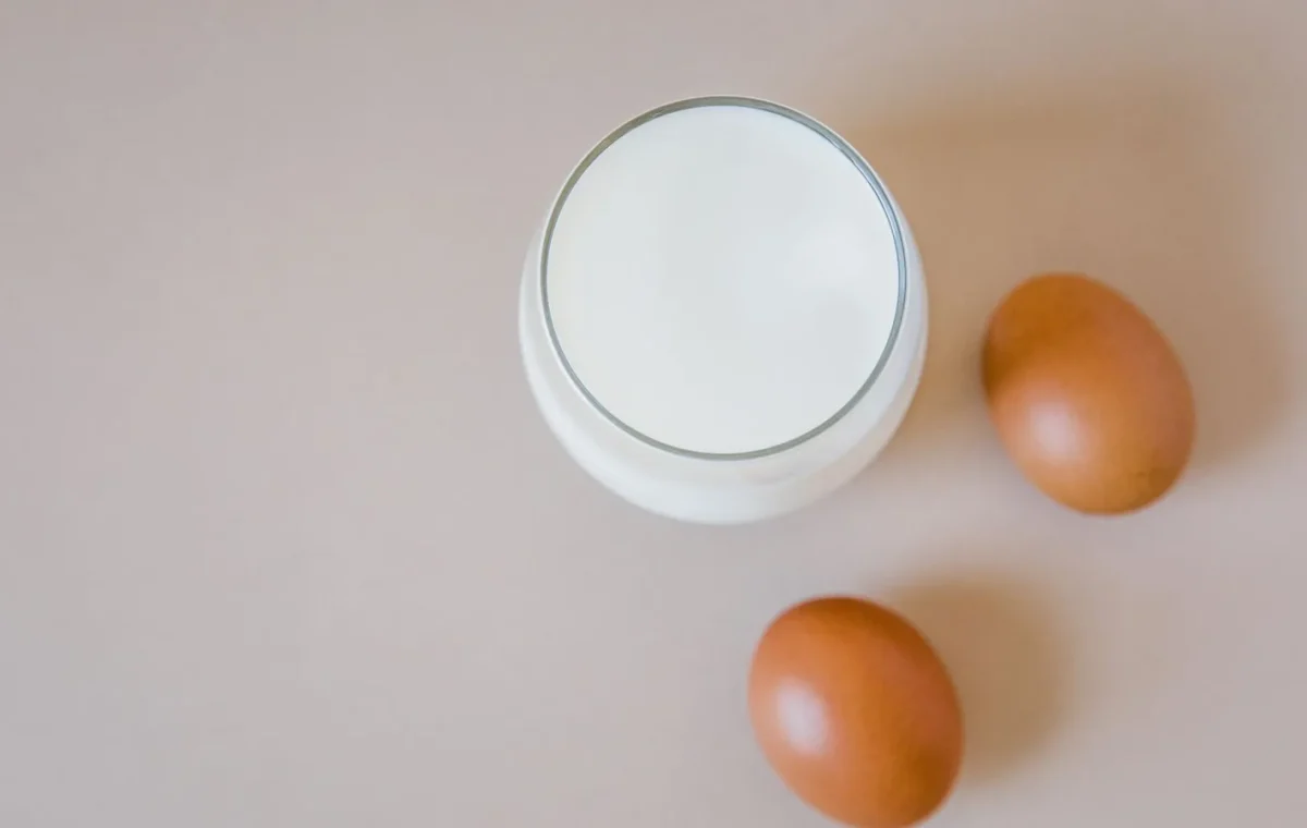 Aesthetic flatlay featuring a glass of milk and two brown eggs on a light surface.