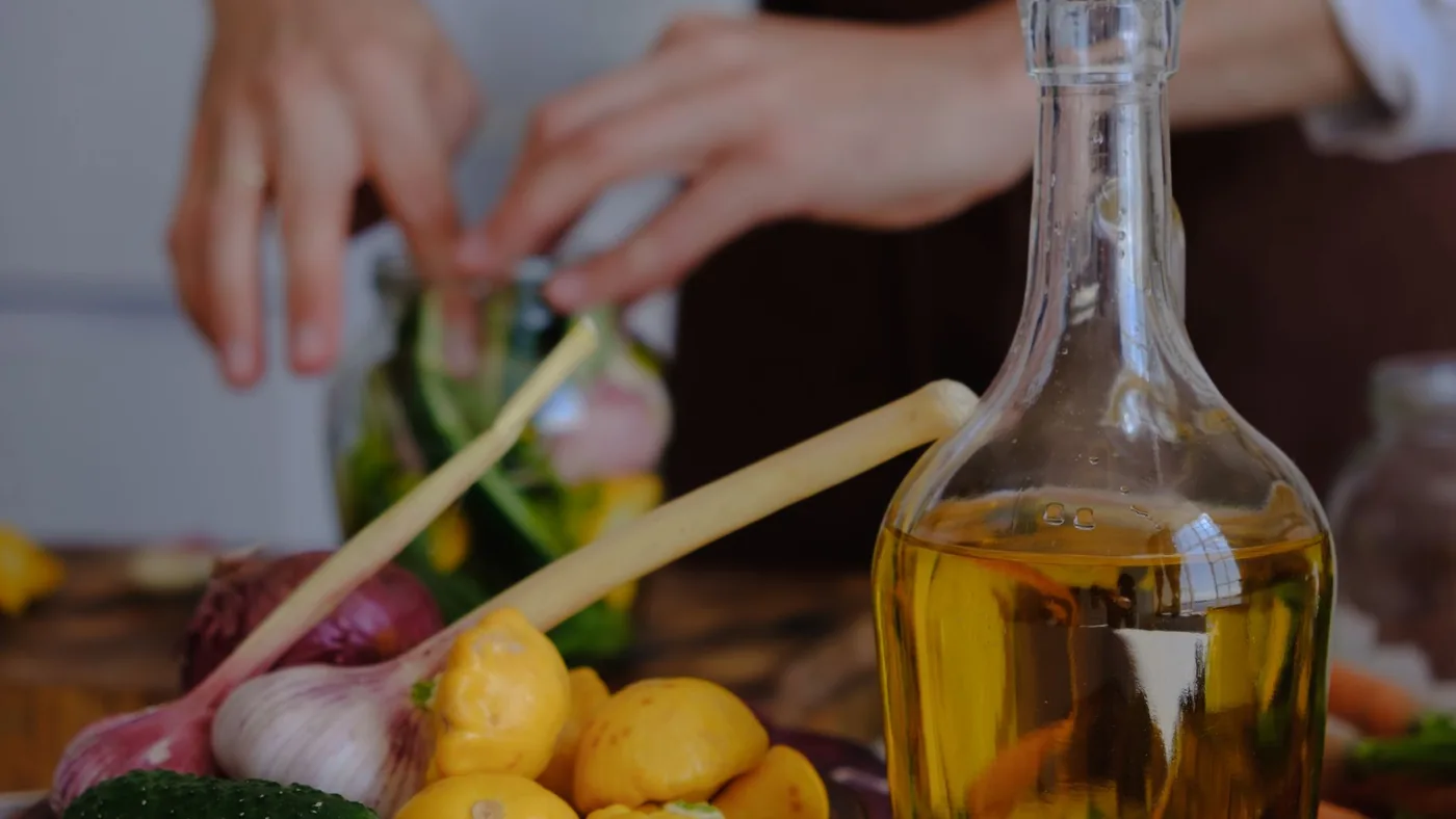 Hands preparing vegetables with olive oil, garlic, and squash in a kitchen setting.